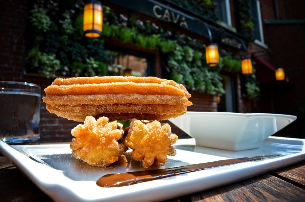 churros on a plate with dipping sauce and a garden and lights behind it.