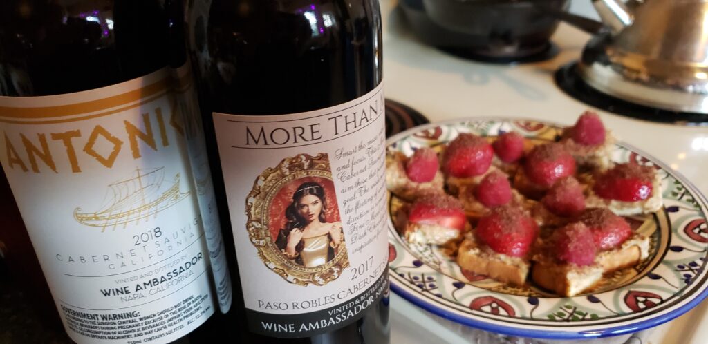 2 red wine bottles next to a plate of almond toast bits with strawberries and resperries sprinkled with dark chocolate. 