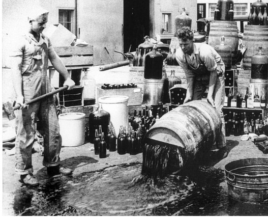 2 men with wine barrels, one is pourong our a barrel. This is during prohibition 1920-1933